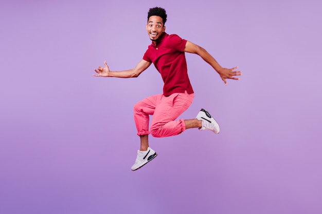 Chico africano deportivo en camiseta casual roja relajante. Modelo masculino positivo con el pelo corto y negro saltando.