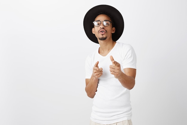 Chico afroamericano descarado guapo hipster con gafas y sombrero señalando con el dedo, felicidades, gesto bien hecho