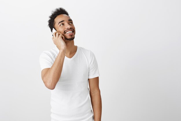 Chico afroamericano despreocupado que mira la esquina superior derecha con una sonrisa feliz mientras habla por teléfono móvil