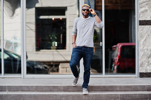 Chico afroamericano con estilo en suéter gris y gafas de sol negras posó en la calle