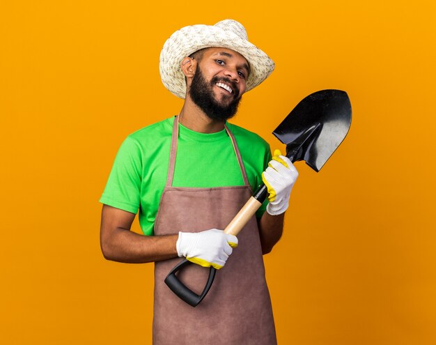 Chico afroamericano joven jardinero confiado con sombrero de jardinería y guantes con pala