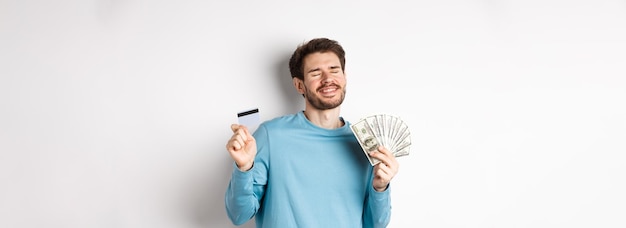 Foto gratuita chico alegre celebrando el salario bailando con tarjeta de crédito de plástico y dinero sonriendo satisfecho suplente