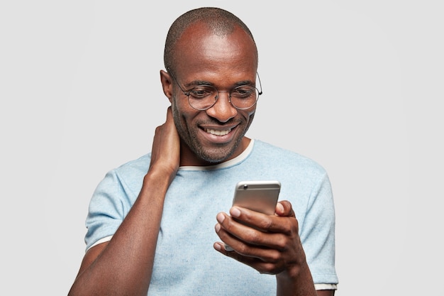 Chico alegre charla en un teléfono inteligente con un amigo o novia, recibe buenas noticias en el mensaje, sostiene un teléfono celular moderno