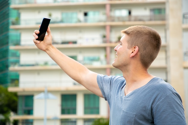 Foto gratuita chico alegre estudiante emocionado tomando selfie al aire libre