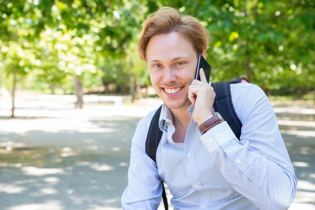 Chico alegre estudiante feliz llamando por teléfono en el parque