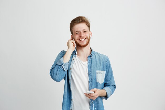 Chico alegre joven en auriculares sonriendo sosteniendo teléfono escuchando música.