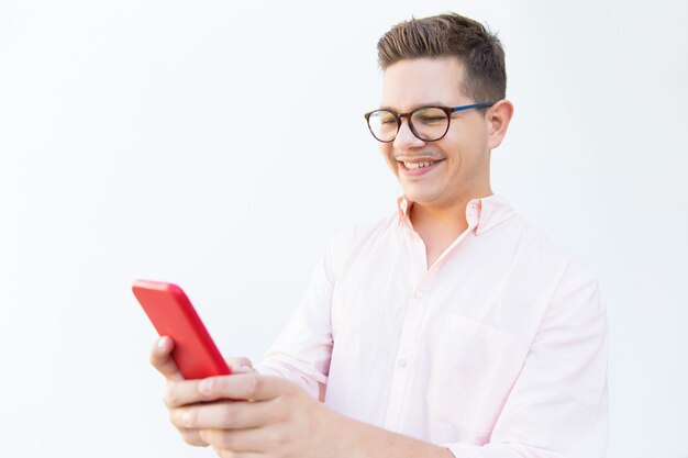 Chico alegre positivo en anteojos leyendo el mensaje en el teléfono