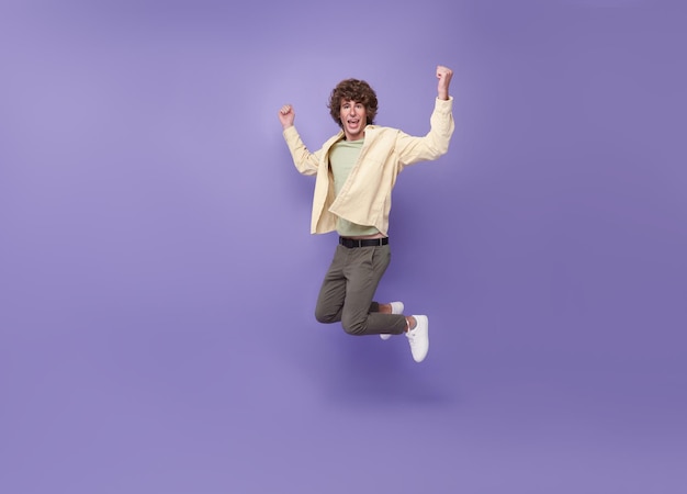 Chico alegre saltando divirtiéndose regocijándose aislado sobre fondo púrpura