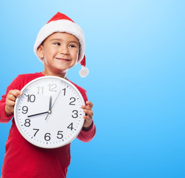 Chico alegre sujetando un reloj blanco con fondo azul