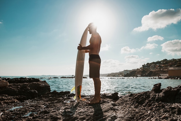 Chico anónimo con tabla de surf en un día soleado