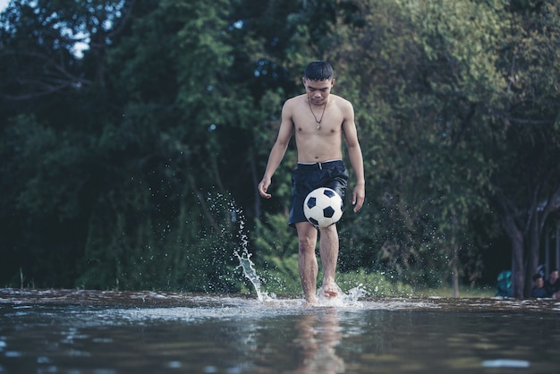 Chico asiático patea una pelota de fútbol en un río