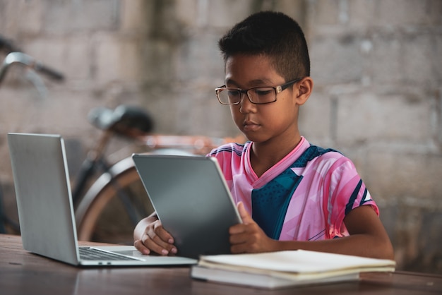 Foto gratuita chico asiático usando la computadora portátil en la mesa, vuelve a la escuela