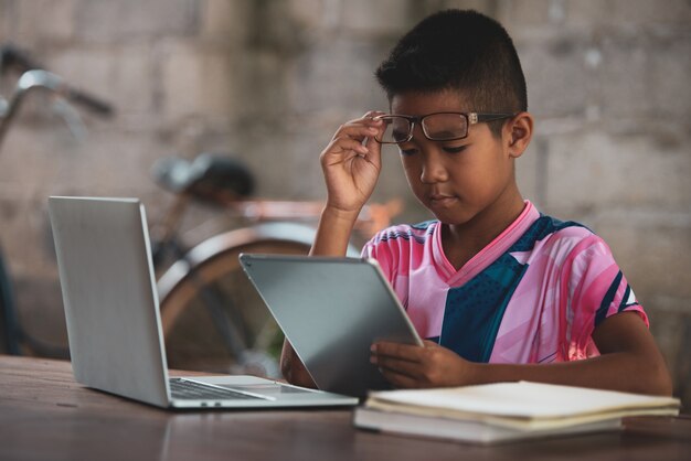 Chico asiático usando la computadora portátil en la mesa, vuelve a la escuela