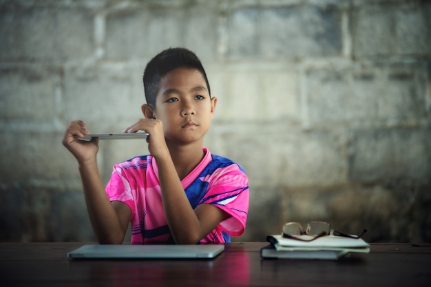 Foto gratuita chico asiático usando la computadora portátil en la mesa, vuelve a la escuela