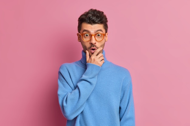 El chico asustado emocionalmente sostiene la barbilla cuando ve algo increíble tiene una cara muy sorprendida