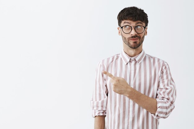 Chico barbudo con estilo curioso posando contra la pared blanca con gafas