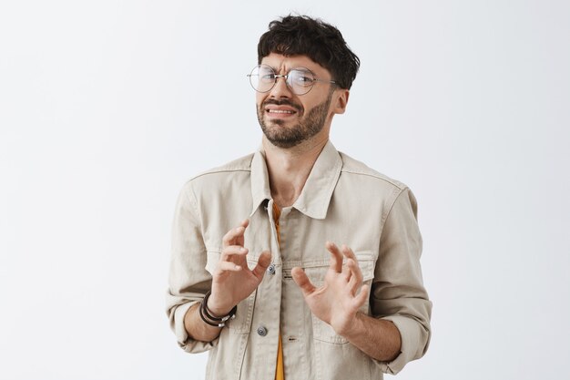 Chico barbudo con estilo disgustado posando contra la pared blanca