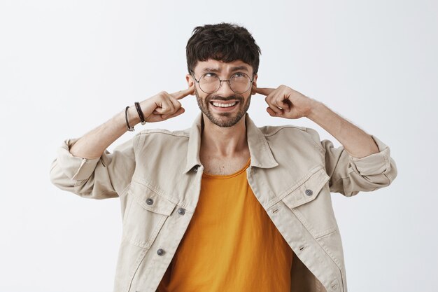 Chico barbudo con estilo molesto posando contra la pared blanca