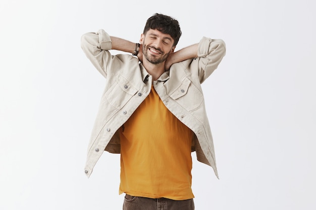 Chico barbudo con estilo relajado posando contra la pared blanca