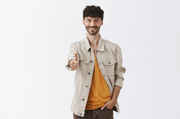 Chico barbudo con estilo satisfecho y seguro posando contra la pared blanca