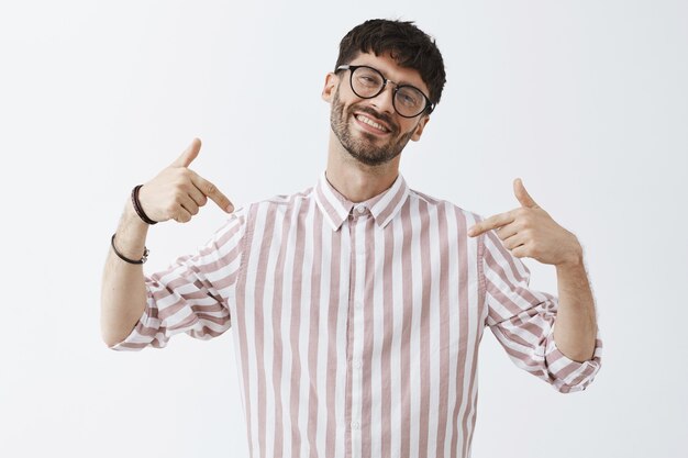 Chico barbudo con estilo seguro posando contra la pared blanca con gafas