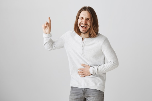 Chico barbudo feliz riendo en promo divertida, apuntando hacia el anuncio