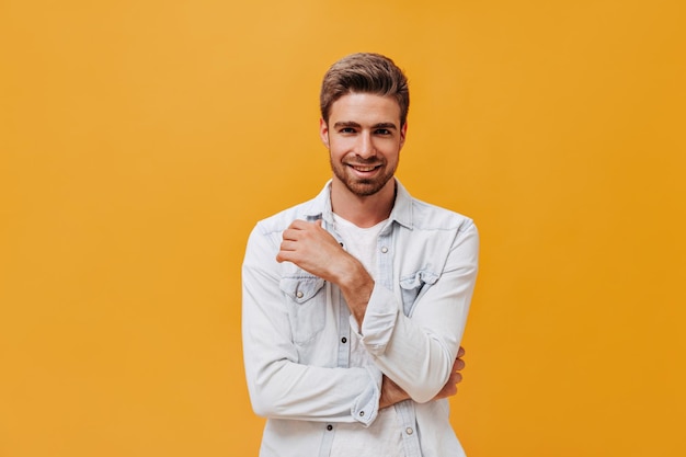 Chico barbudo de moda con peinado elegante en chaqueta blanca moderna sonriendo y mirando a la cámara en un contexto aislado