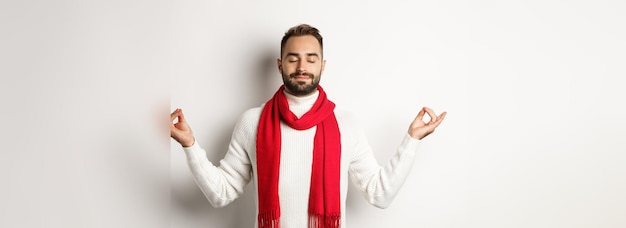 Foto gratuita chico barbudo relajado de pie en paz meditando con los ojos cerrados de pie sobre fondo blanco en