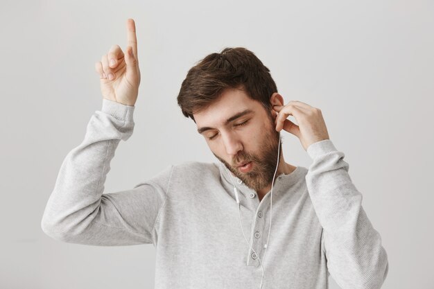 Chico barbudo tonto despreocupado escuchando música en auriculares y bailando