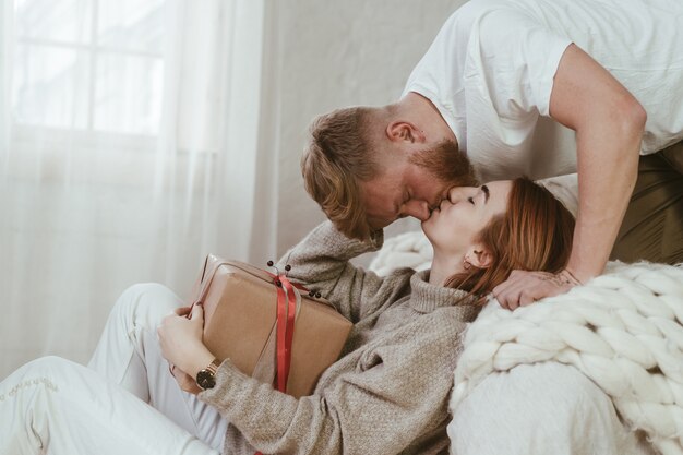 El chico de la cama besa a una chica que se sienta en el suelo