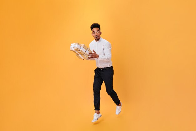 Chico con camisa blanca y pantalón negro rebota con regalos