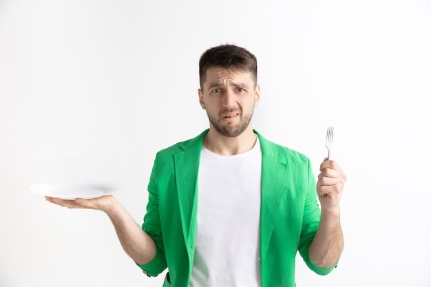 Chico caucásico atractivo triste joven con plato vacío y tenedor aislado sobre fondo gris. Copie el espacio y simule. Fondo de plantilla en blanco. Rechazo, concepto de rechazo