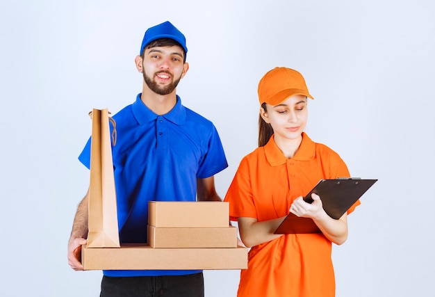 Chico y chica mensajero con uniformes azules y amarillos sosteniendo cajas de cartón para llevar y paquetes de compras y presentando la lista de clientes.