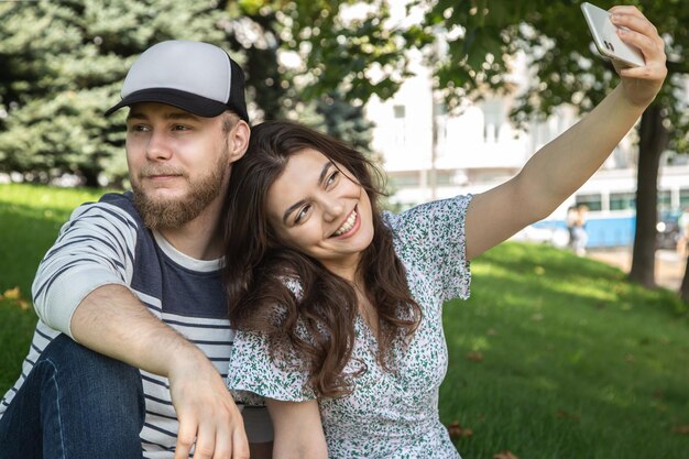 Un chico y una chica se toman un selfie sentados en el césped del parque