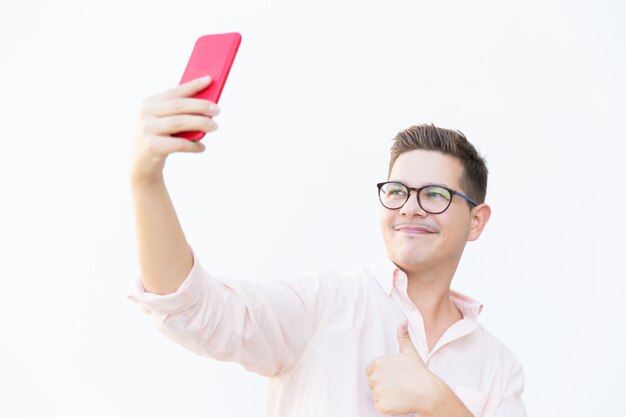 Chico contento con anteojos haciendo gestos y tomando selfie