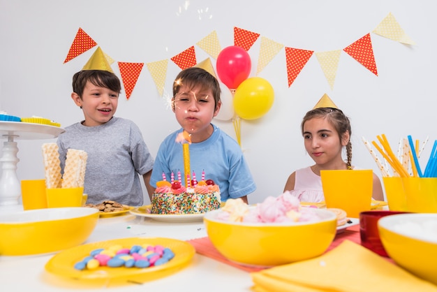 Chico de cumpleaños soplando velas con sus amigos