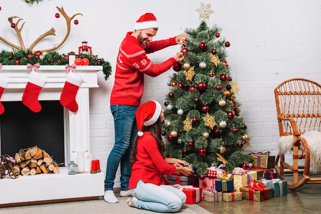 Chico y dama decorando arbol de navidad con adornos.