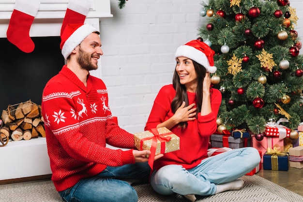 Chico dando presente a la señora cerca del árbol de navidad