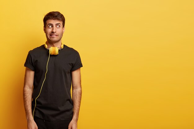 Chico desconcertado con cabello oscuro, dientes apretados, mira sospechosamente a un lado, usa camiseta negra