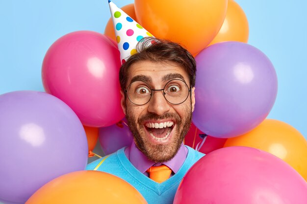 Chico divertido feliz rodeado de globos de fiesta posando