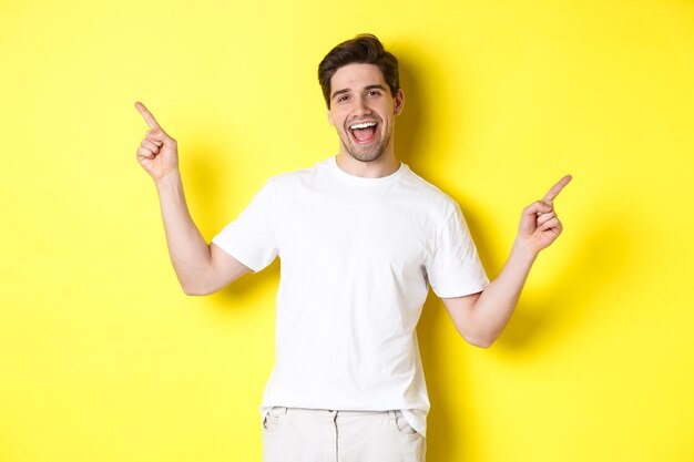 Chico elegante feliz mostrando dos variantes, señalando con el dedo hacia los lados en la promoción izquierda y derecha, de pie sobre fondo amarillo.