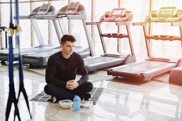 Chico elegante en el gimnasio, relajarse en el piso y comer alimentos saludables.