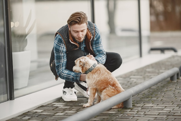 Chico elegante jugando con un perro. Hombre en la ciudad de otoño.