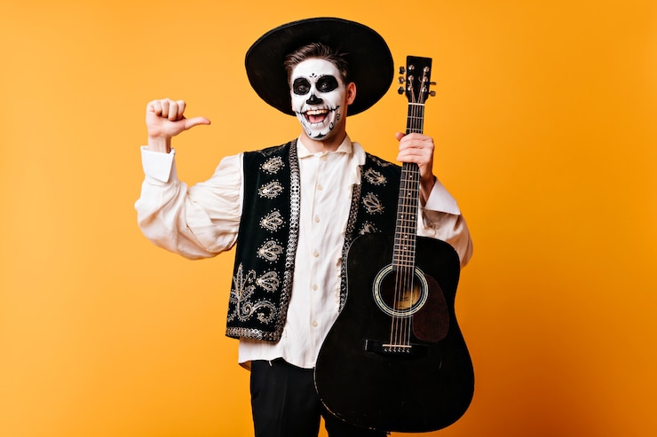 Foto gratuito chico emocionado en ropas tradicionales mexicanas con guitarra. feliz cantante muerto divirtiéndose en la fiesta de halloween.