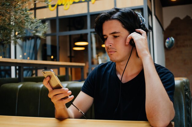 Chico escuchando música con auriculares en una cafetería.