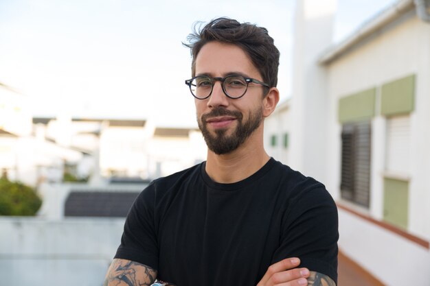 Chico con estilo alegre en gafas posando en el balcón del apartamento