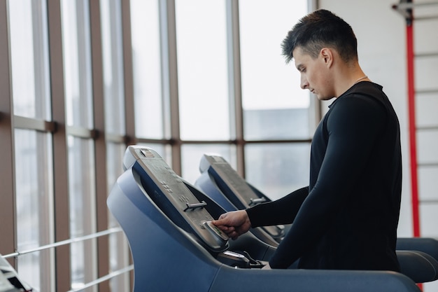 Un chico con estilo en el gimnasio está entrenando en la cinta. Estilo de vida saludable.