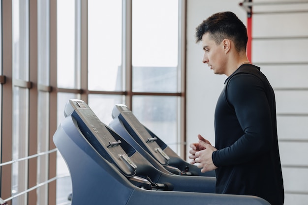 Un chico con estilo en el gimnasio está entrenando en la cinta. Estilo de vida saludable.