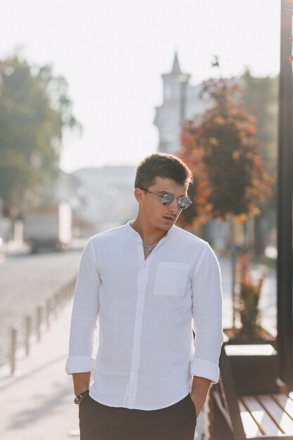 Chico con estilo joven en una camisa caminando por una calle europea en un día soleado