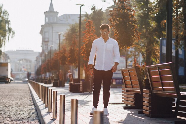 Chico con estilo joven en una camisa caminando por una calle europea en un día soleado